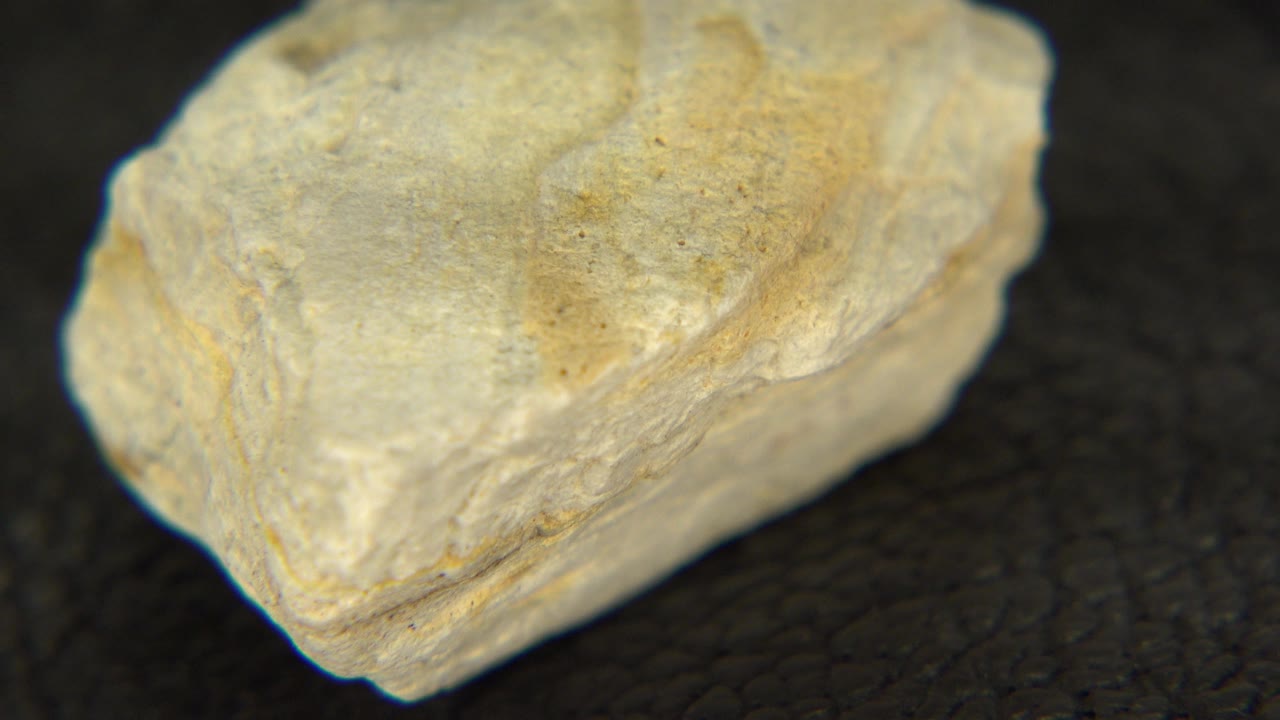 At 0:01, the yellow stone remains in close-up on the dark surface, showing a broad flat top and rough layered side, with no visible people.