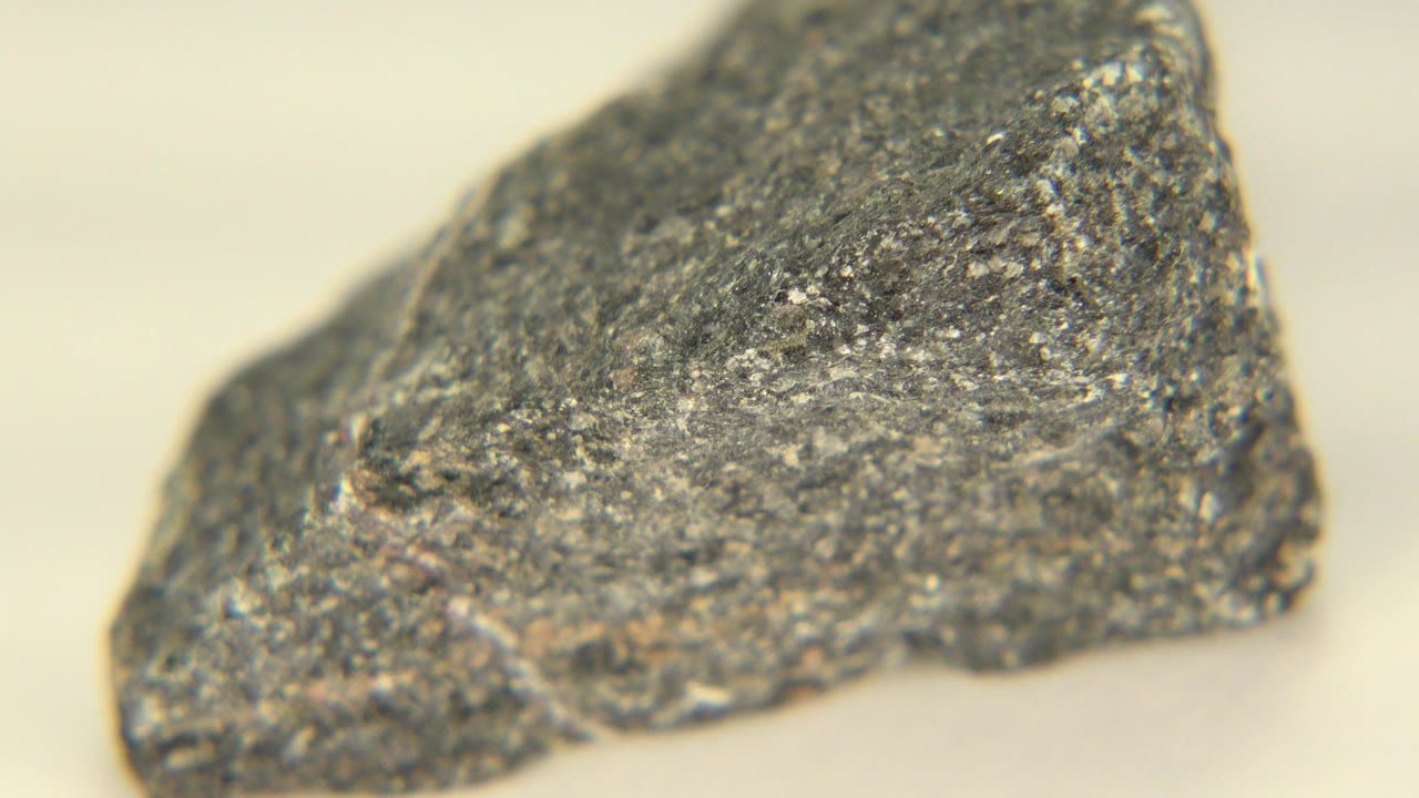 Close-up of an angular gray fractured rock on a pale surface in Westminster, Colorado, with small reflective flecks and no visible people.