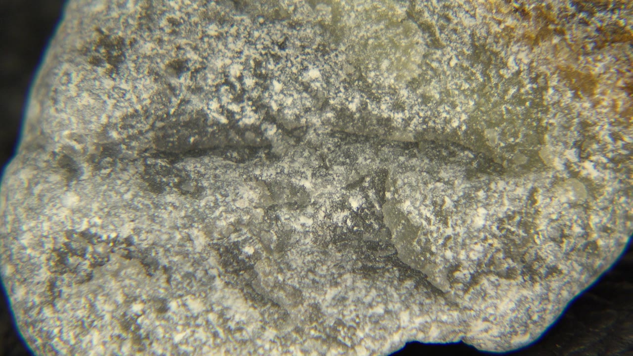 The stone remains large in frame at 0:01, showing a flatter face with speckled gray texture, tan edges, and no visible people.