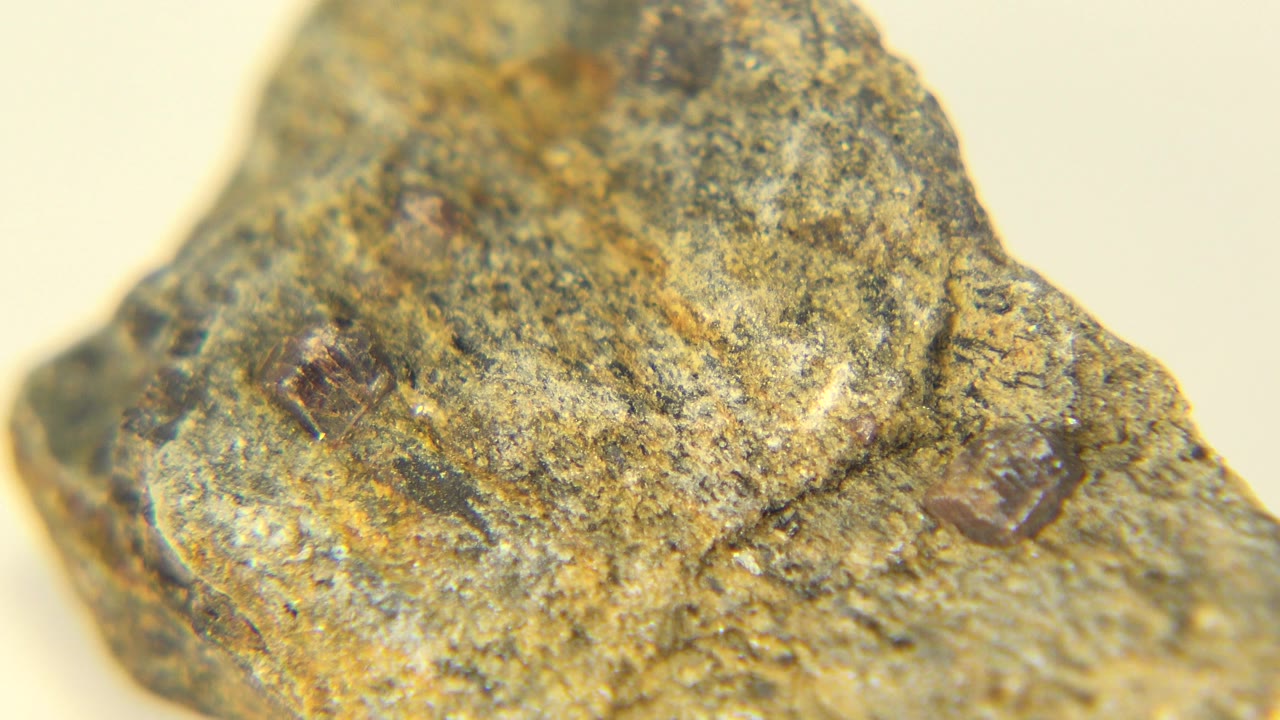 Angled close-up of a rough rock sample with reddish mineral spots.