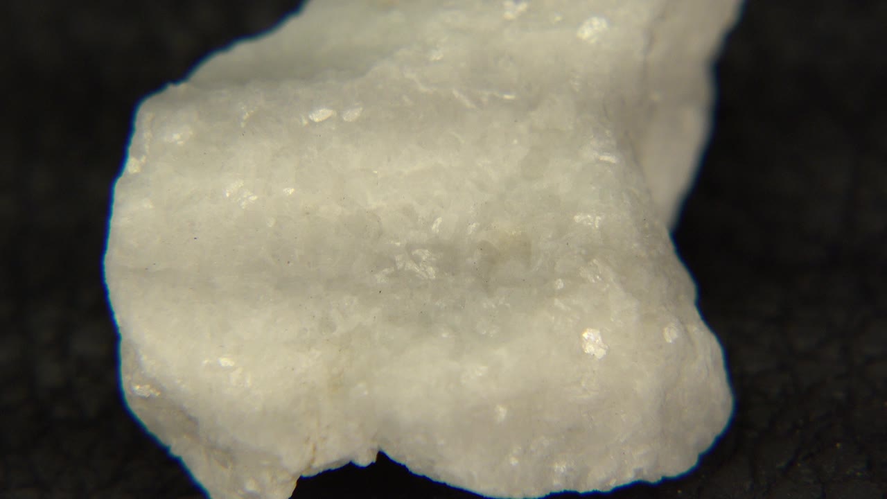 A pale irregular rock fills the upper-left frame on a dark table in Westminster, Colorado footage, with no visible people.