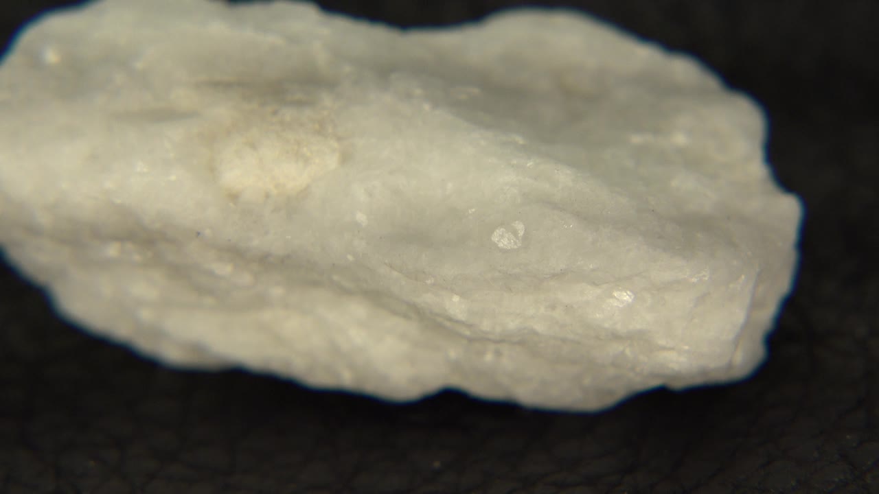 The pale stone appears longer across the frame on a black background, with small reflective flecks visible and no visible people.