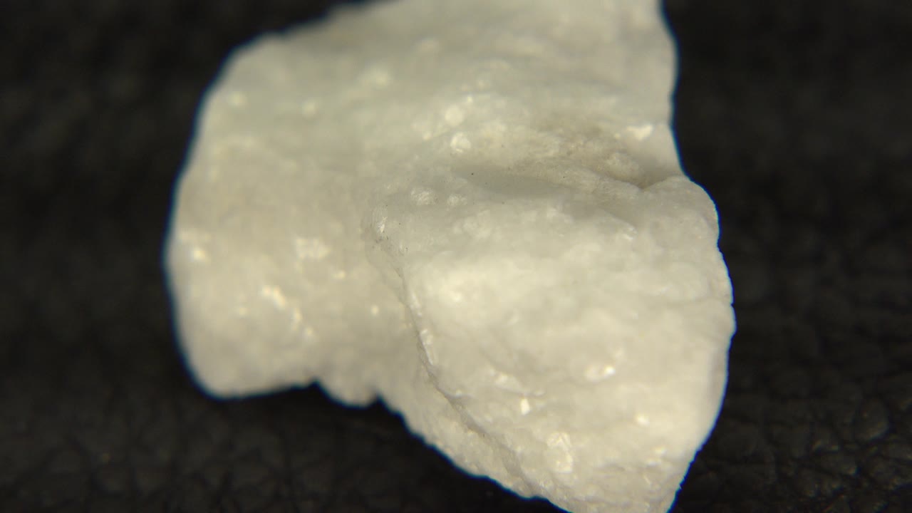 At 0:00, a white irregular rock sits large in frame on a dark speckled tabletop in Westminster, Colorado, with no visible people.