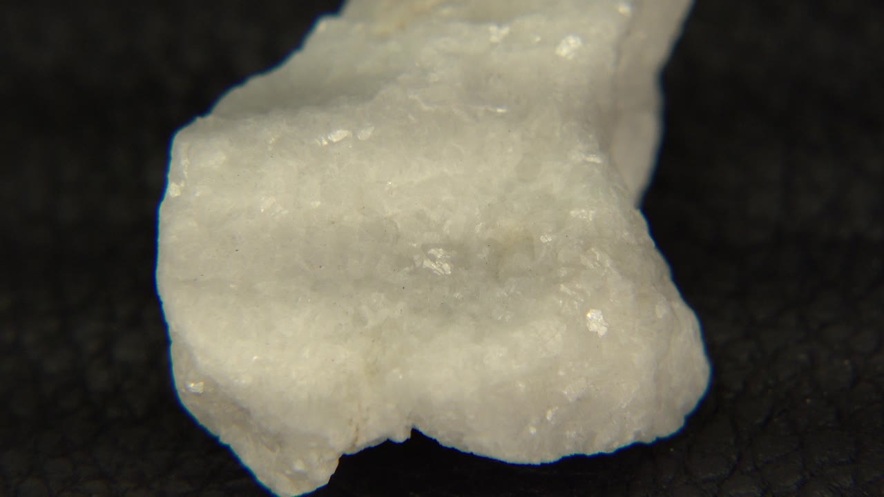 The white crystal rock remains close and centered on the black felt, showing a broad pale face and small sparkling flecks, with no visible people.
