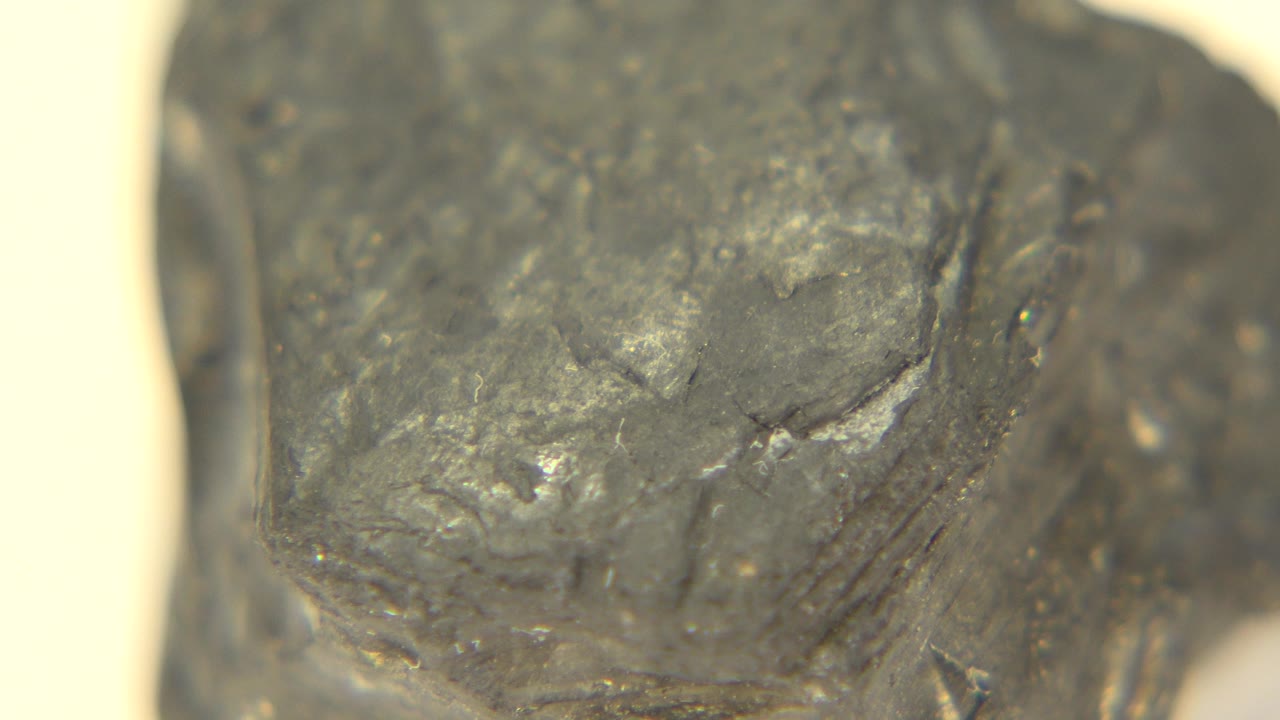 A slightly shifted close view of the graphite rock shows a broad dark face with small reflective flecks and rough cracks in Westminster, Colorado, no visible people.