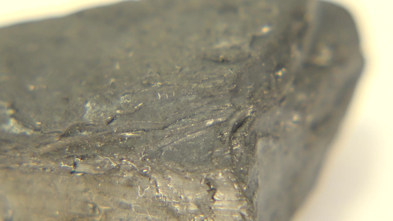 Extreme close view of a dark gray rock on a warm light tabletop in Westminster, Colorado, with the upper face angled across the frame and no visible people.