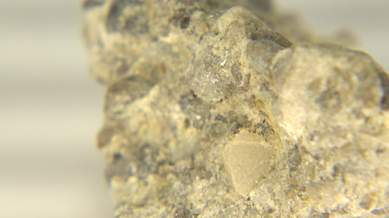 Close view of the rock one second in, showing a pale translucent patch surrounded by speckled gray and tan material, with no visible people.