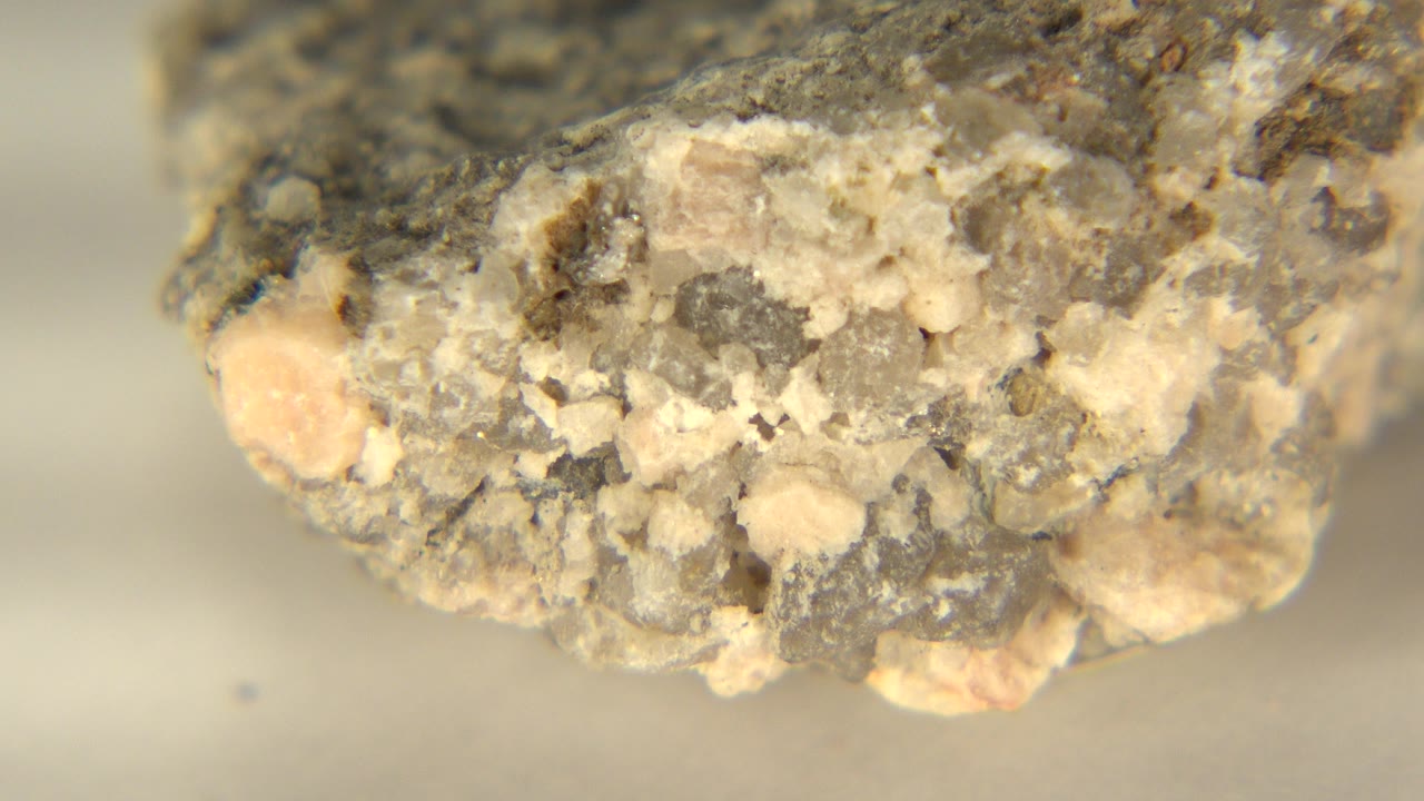 At 0:00, a light-colored coarse rock edge fills the upper frame in Westminster, Colorado, with tan crystals, gray grains, and no visible people.