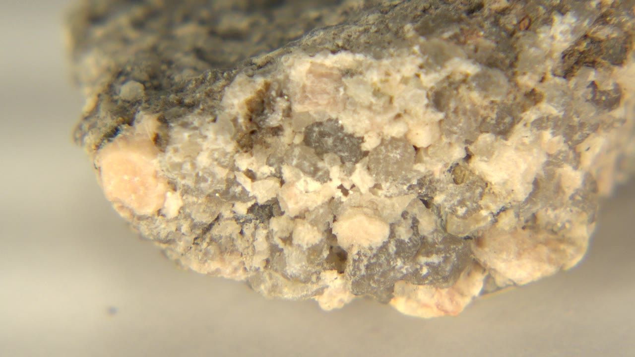 At 0:01, the close rock face remains centered in Westminster, Colorado, showing cream and gray crystalline grains with a soft pale background and no visible people.