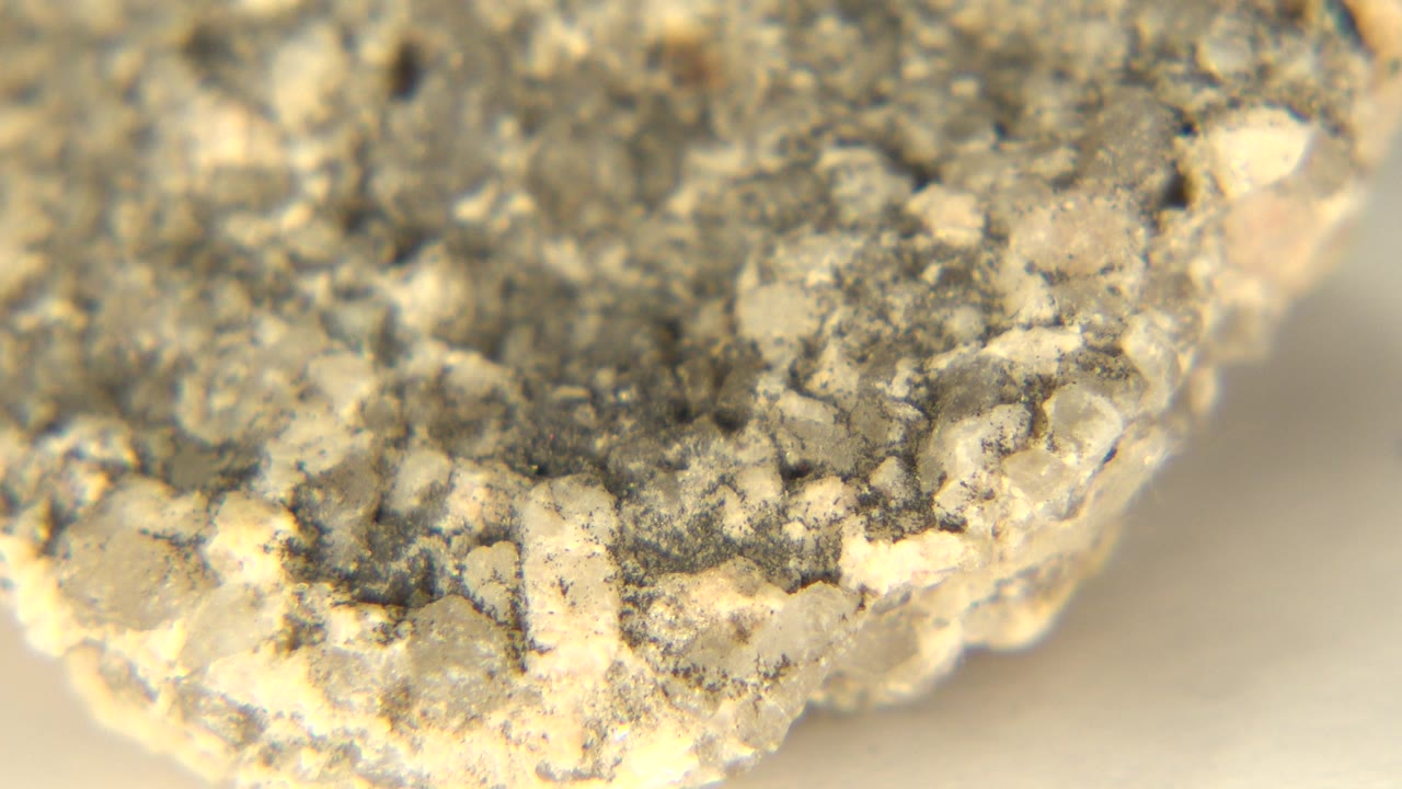 At 0:01, the rock surface remains close to camera in Westminster, Colorado, showing darker gray grit, beige inclusions, yellow sand, and no visible people.