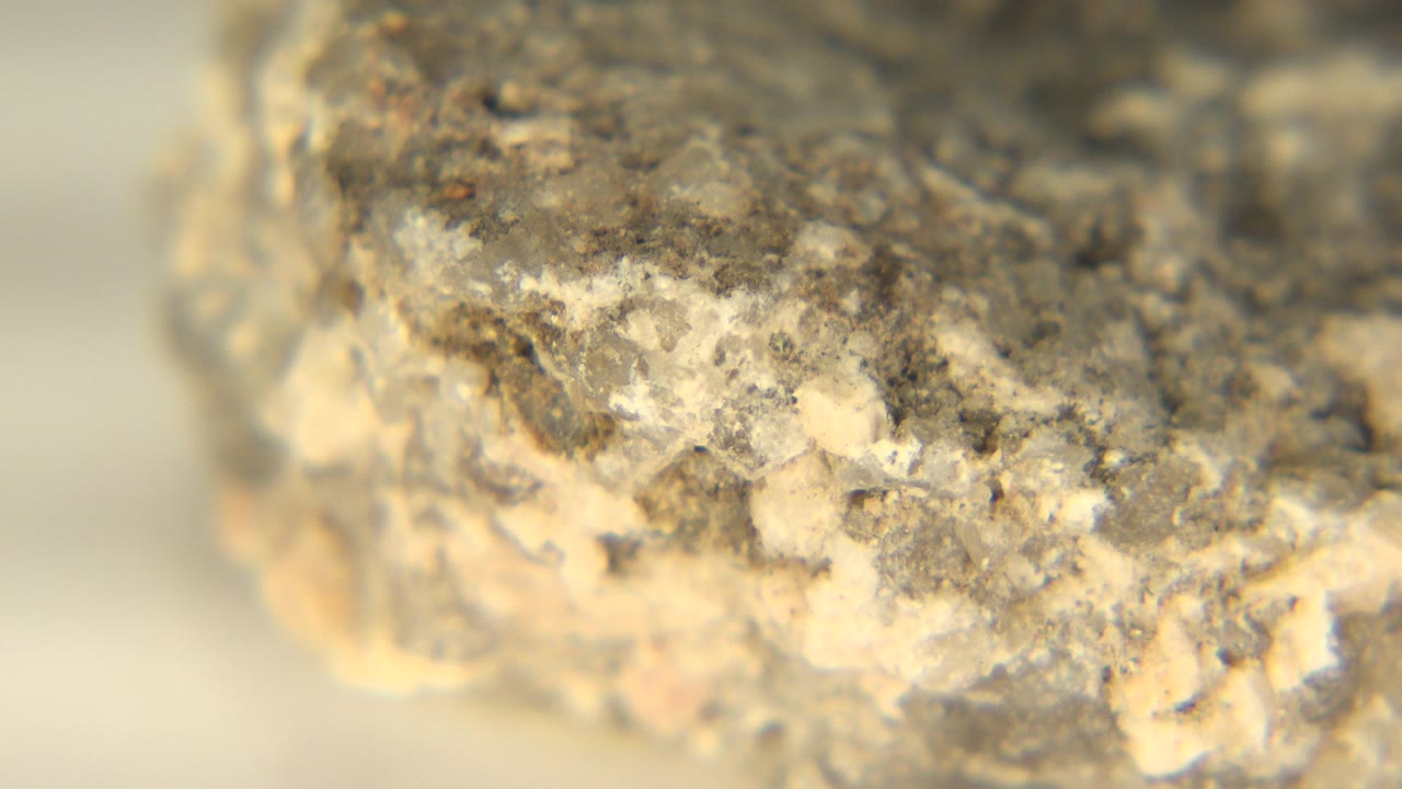 At 0:01, the camera view remains close on the rock edge, showing pale mineral flecks and gray grit on the white floor in Westminster, Colorado, with no visible people.