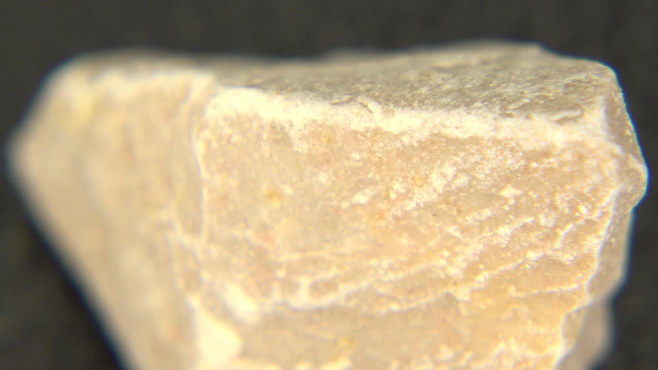 A close view of the tan rock face shows a bright worn top edge and granular surface detail in Westminster, Colorado, with no visible people.