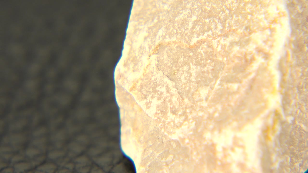 Close-up of a pale gray stone on a dark textured surface.