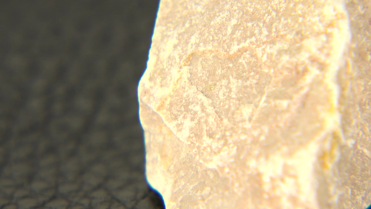 At 0:01, the stone remains in extreme close-up in Westminster, Colorado, showing a flatter chipped face and powdery beige-gray texture with no visible people.