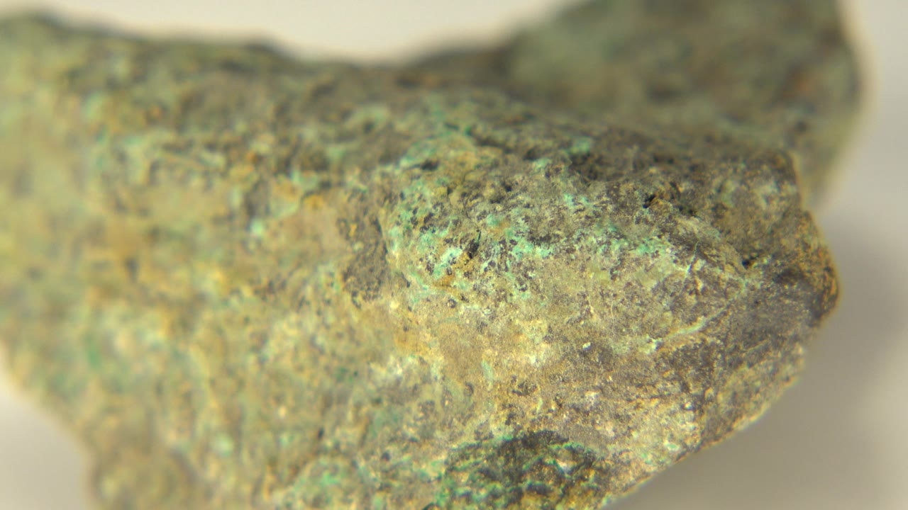 Second close frame of the Westminster rock specimen, showing mottled green mineral flecks across a tan-gray surface with no visible people.