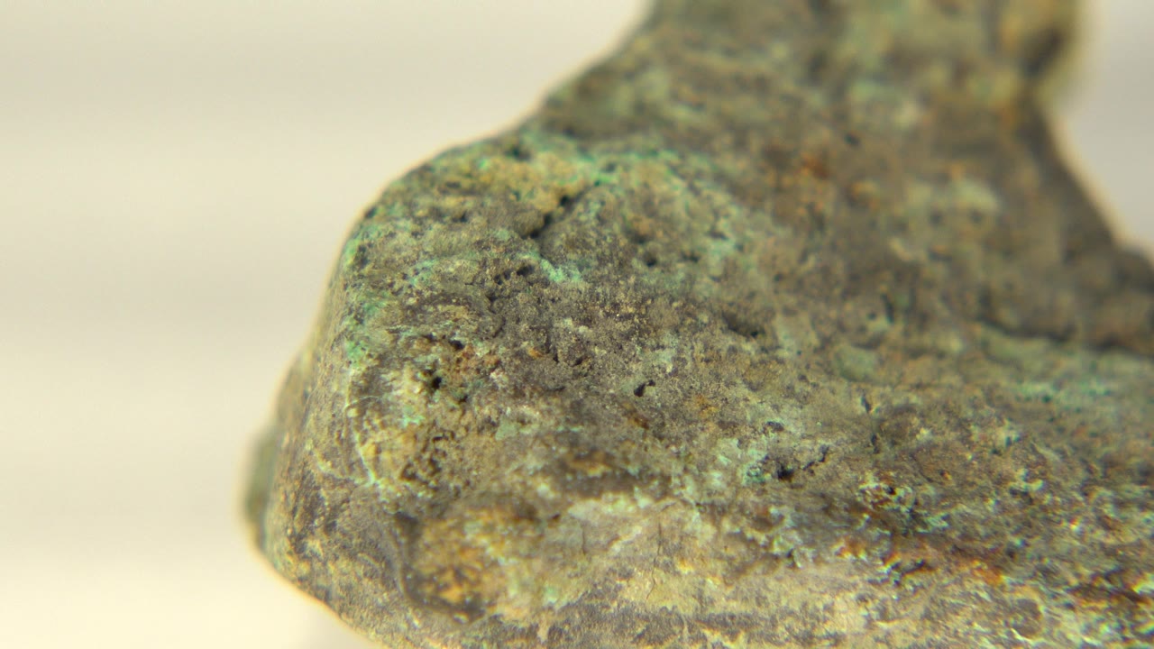 Extreme close-up of a rough green and brown cave rock in Westminster, Colorado, with a pale blurred background and no visible people.