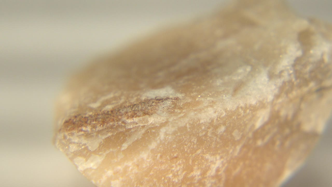 The rotating rock shows a broader pink beige face with a brown internal streak and soft highlights, filmed in Westminster, Colorado, with no visible people.