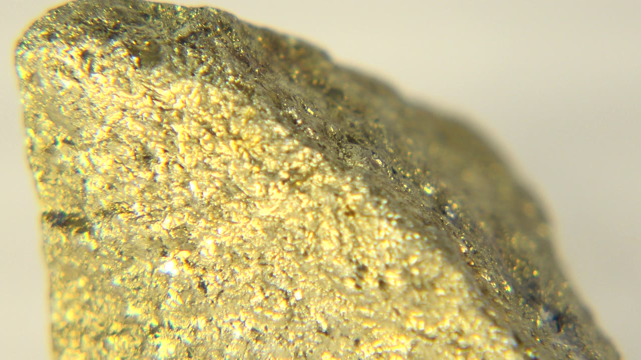 Close-up of the upper edge of a gold-colored nugget in Westminster, Colorado, with bright white light reflecting off rough metallic texture and no visible people.