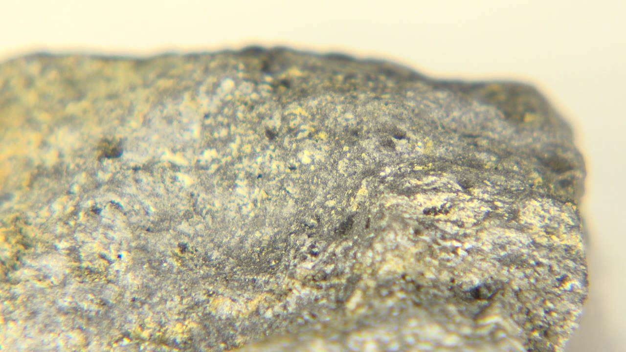 Close-up start frame of a rough gray and tan rock filling the foreground on a pale table in Westminster, Colorado, with no visible people.