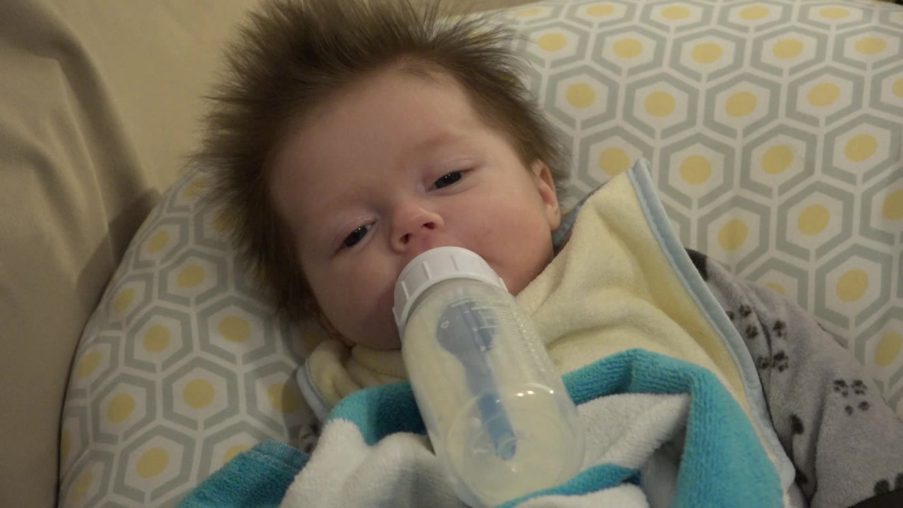 Baby lying on a patterned pillow with a bottle in their mouth.