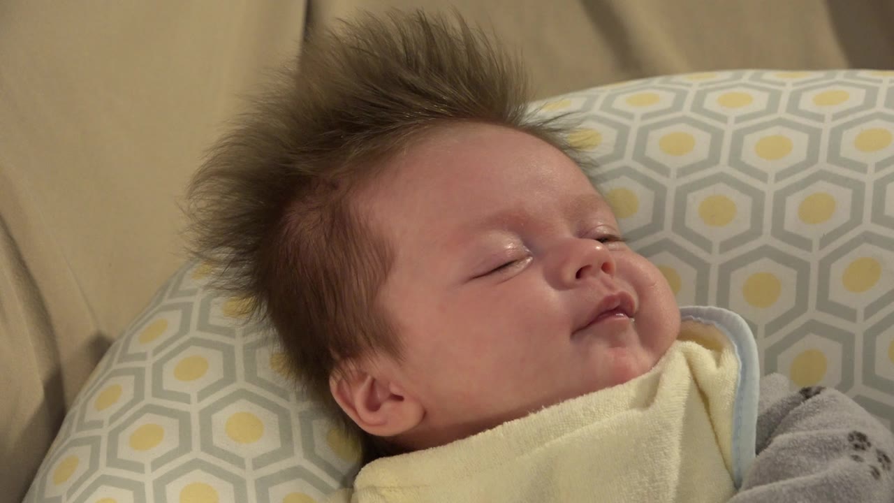 The infant remains asleep in a tight Westminster, Colorado close-up, with the face angled slightly upward and the patterned cushion behind the head.