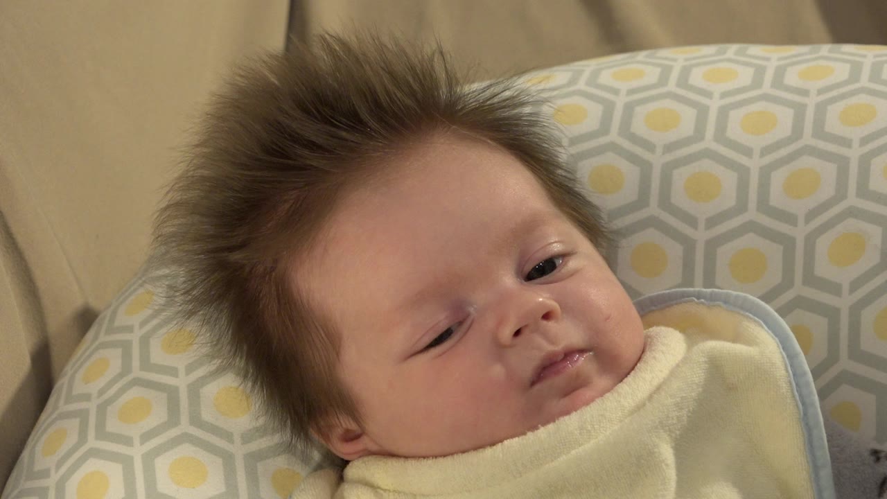 Baby with tousled hair lying on a patterned pillow.