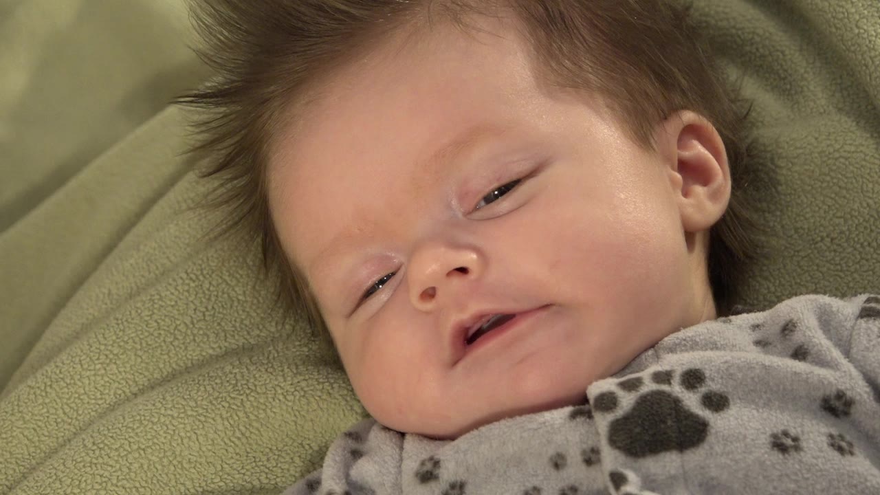 Baby on blanket with mouth slightly open and eyes narrowing.