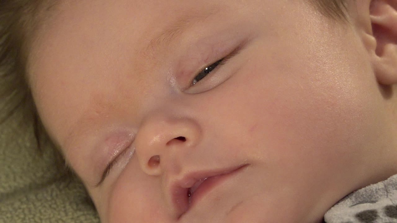 Close-up of a sleepy baby's face with one eye partly open.