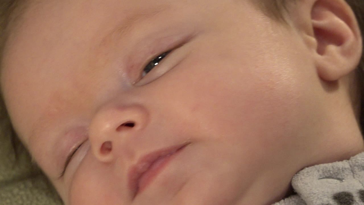 Sleeping infant face in close-up with one eye partly open.
