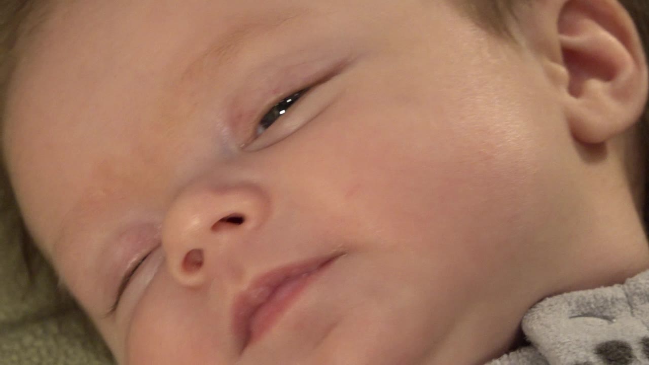 The infant remains reclined in Westminster, Colorado, with eyelids heavy and the cheek, ear, and patterned shirt edge visible.