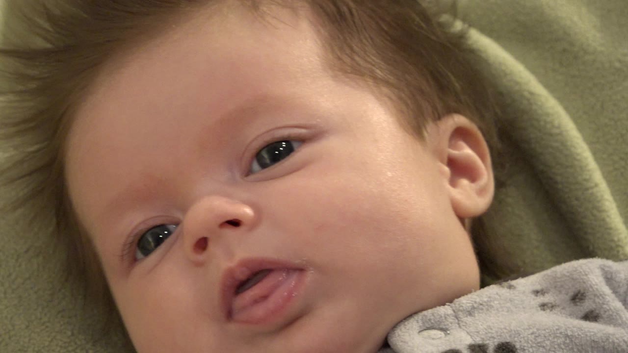 Close-up baby with tongue slightly out on green fabric.