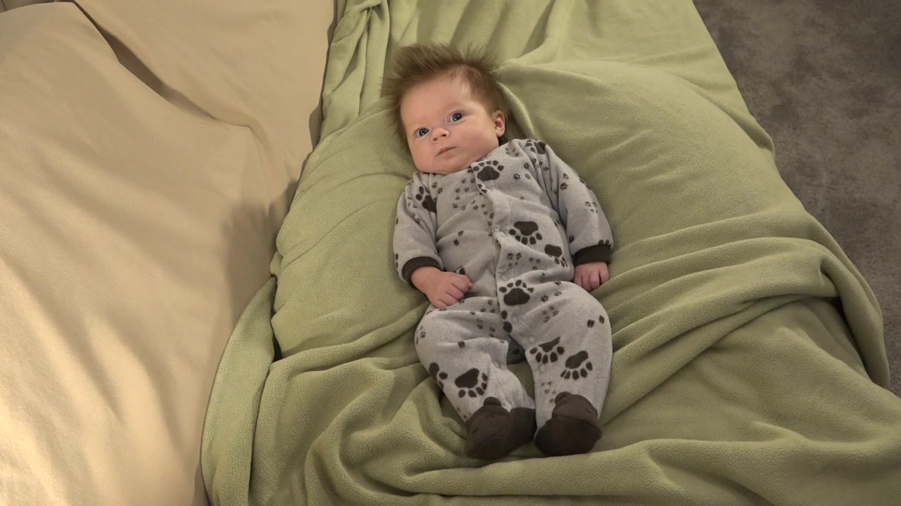 Baby lying on a green blanket beside cream bedding.