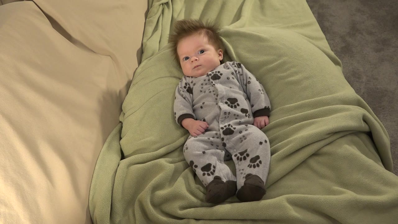 One second in, the baby remains on the green blanket in Westminster, Colorado, looking upward with cream bedding still visible along the left side.