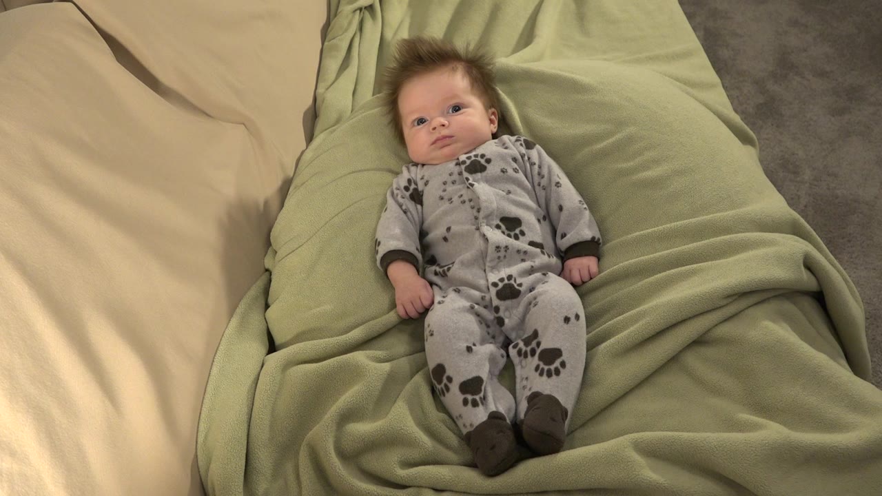 Baby lying on green bedding in grey pajamas.