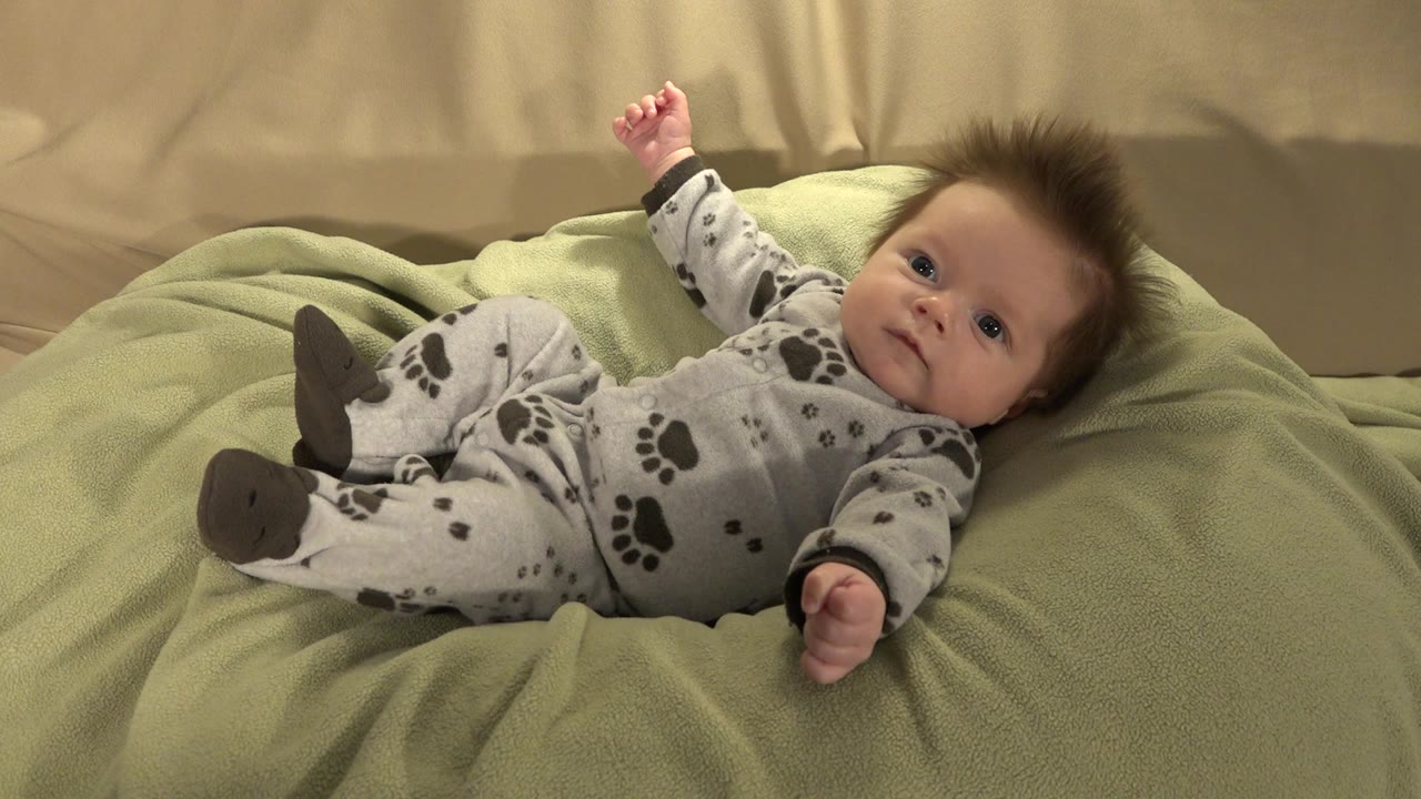 Baby lying on a green puff with one arm raised.