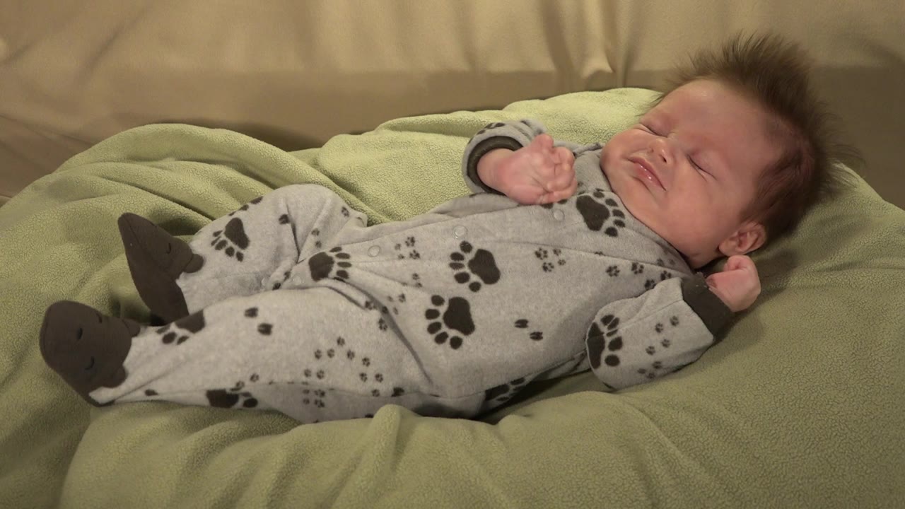 Baby lying with eyes closed on a green blanket.