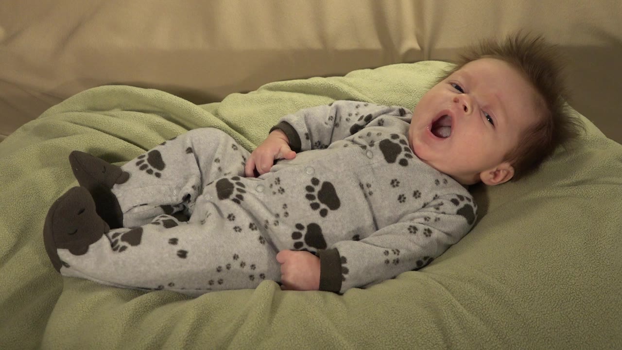 Baby lying on a green blanket with mouth open.