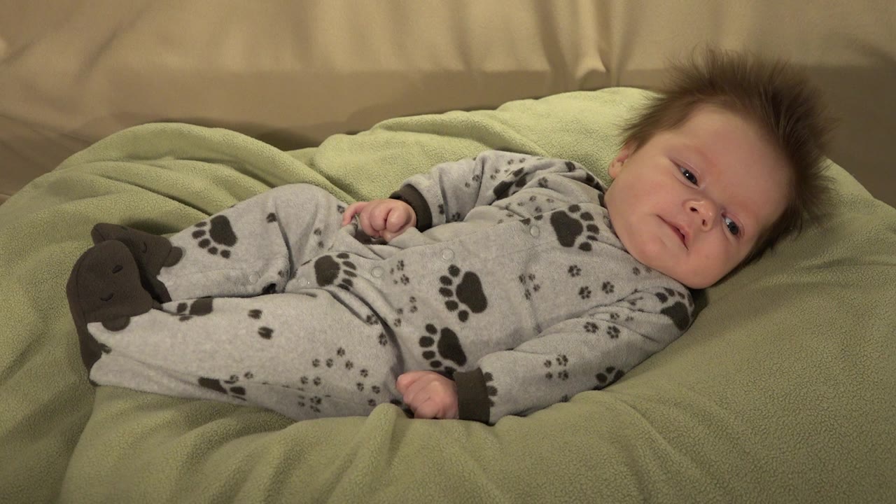 Baby lying on a green blanket in a gray paw-print sleeper.