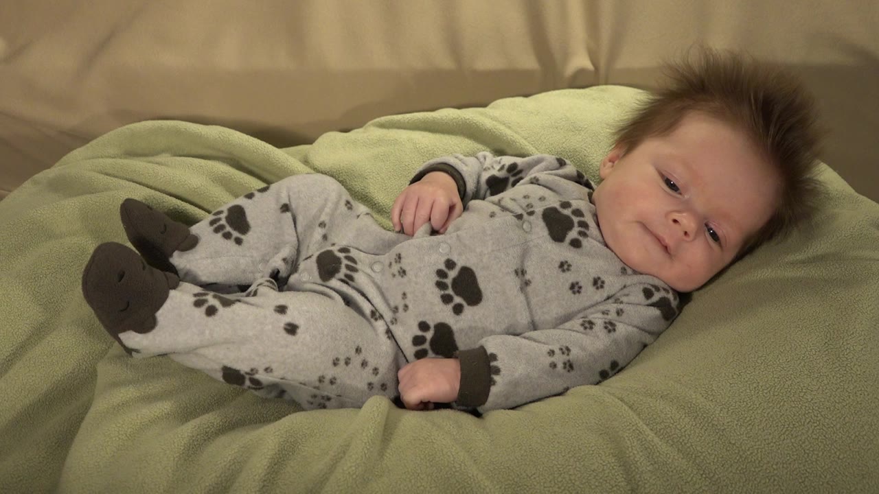 Baby lying on a green cushion in a gray paw-print sleeper.