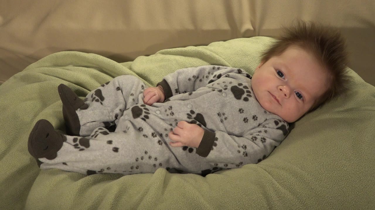 Baby lying on a green blanket in a gray paw-print sleeper.