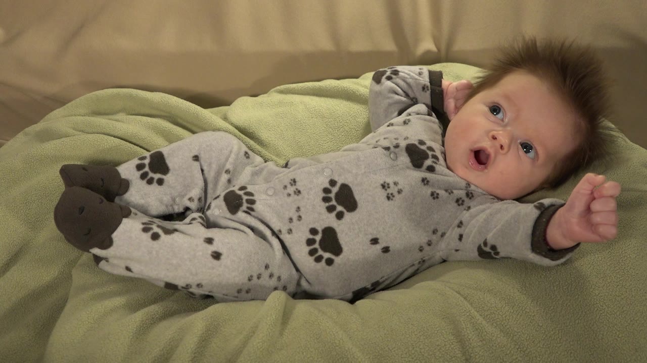 Infant lying on a green pillow in a gray animal-track jumpsuit.