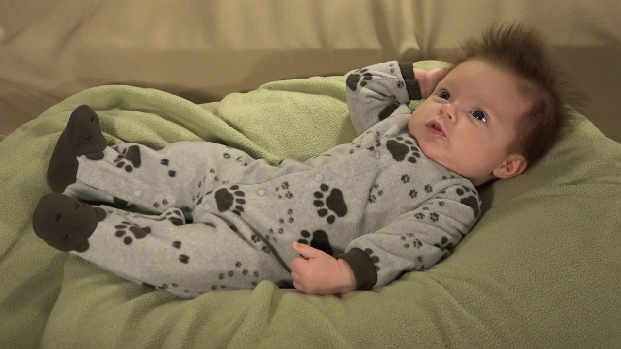 Baby boy lying on a green cushion in a gray paw-print sleeper.