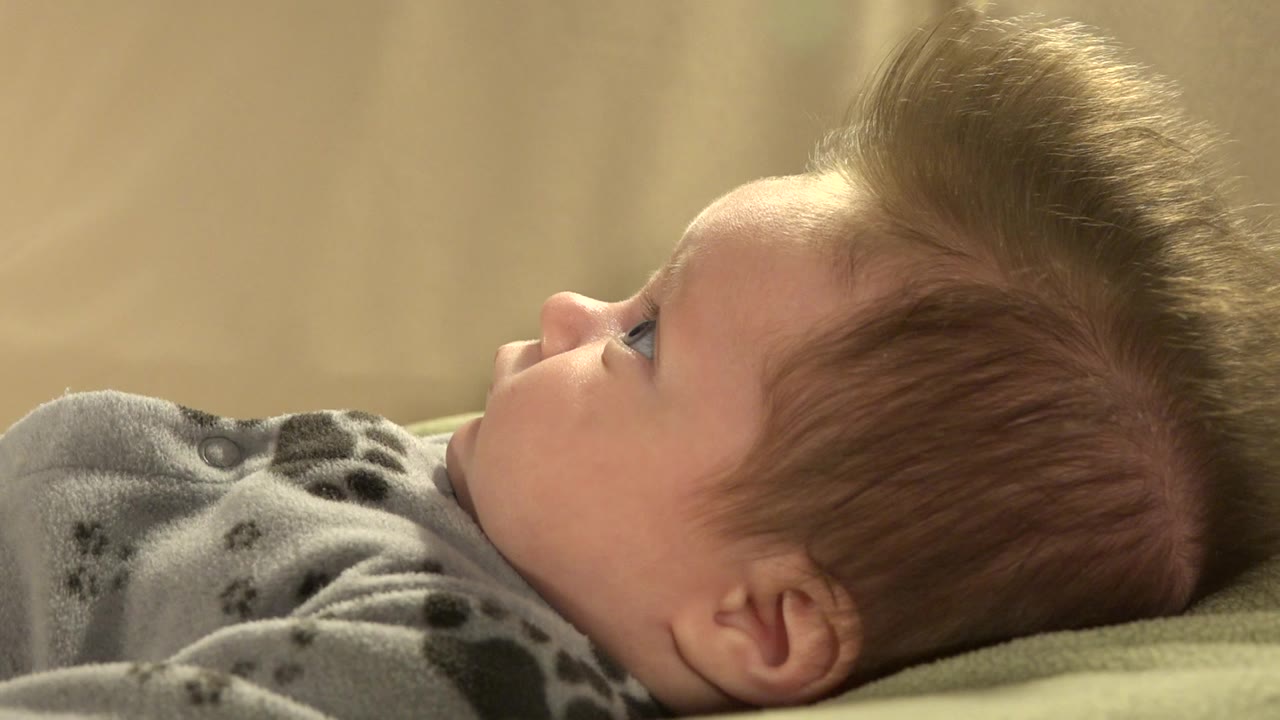 Brown-haired baby lying on back in gray outfit