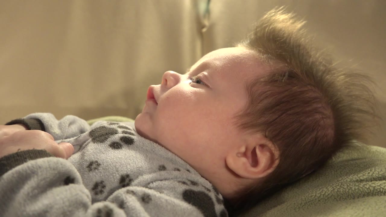 At 0:01, the child remains in side profile on the bed in Westminster, Colorado, with the face angled slightly upward and the gray sleeper visible in the foreground.