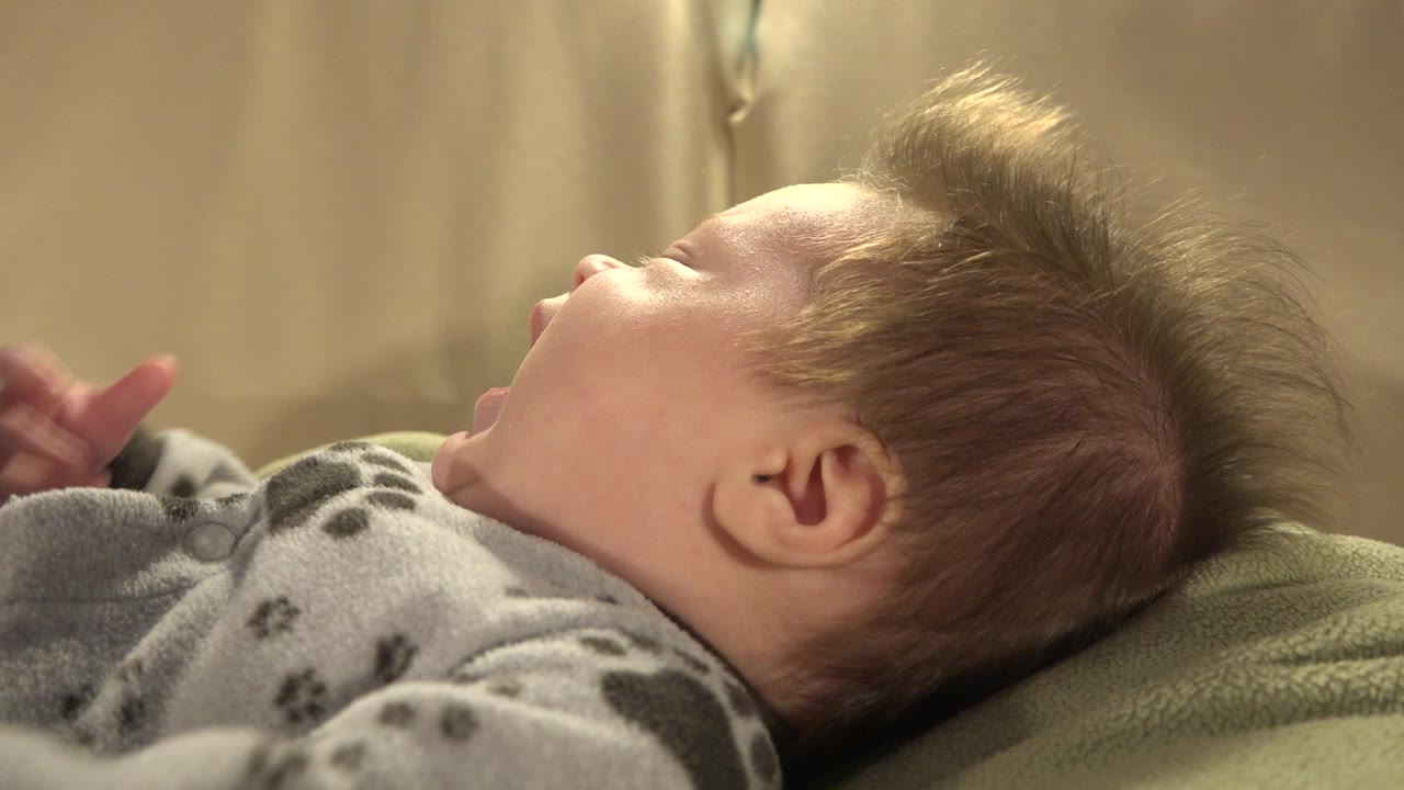 Baby with blond spiky hair lying on a green cushion.