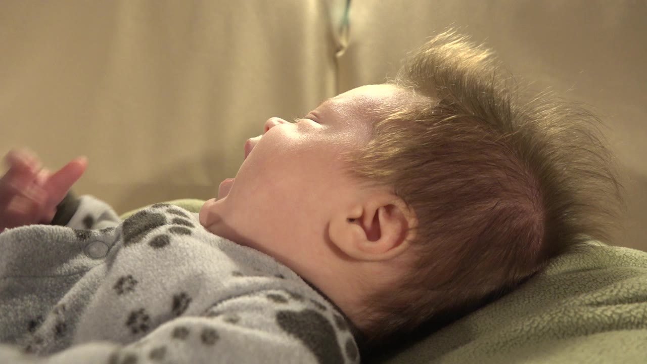 In Westminster, Colorado, the baby remains in side profile with blond hair lifted upward, a gray patterned sleeper visible, and warm light falling across the face.