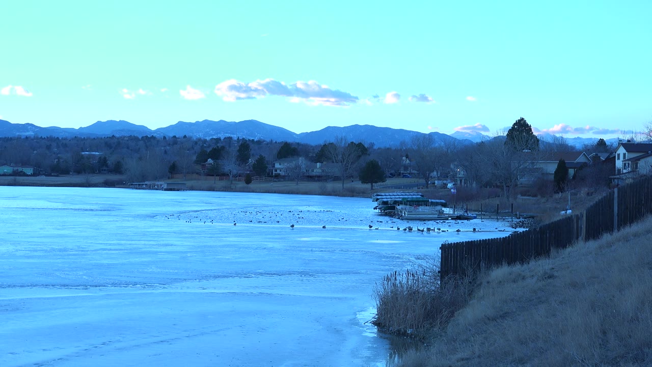 Wide lake and mountain view with homes and a dock along the far shore.