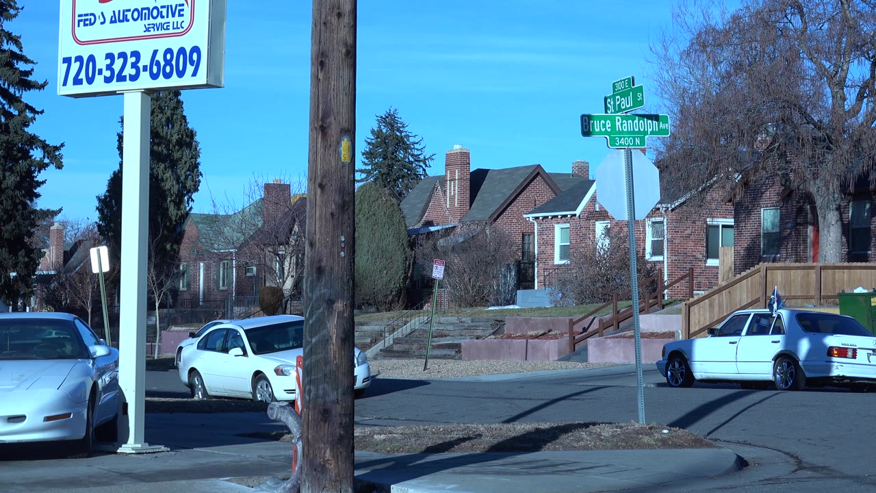 Denver street view with the Bruce Randolph Avenue and Saint Paul Street signs above parked cars, brick houses, bare trees, and no clearly visible people.