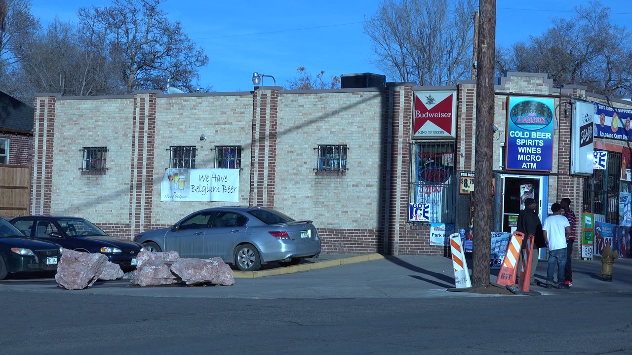 Store entrance with parked cars, signs, and people near the doorway.