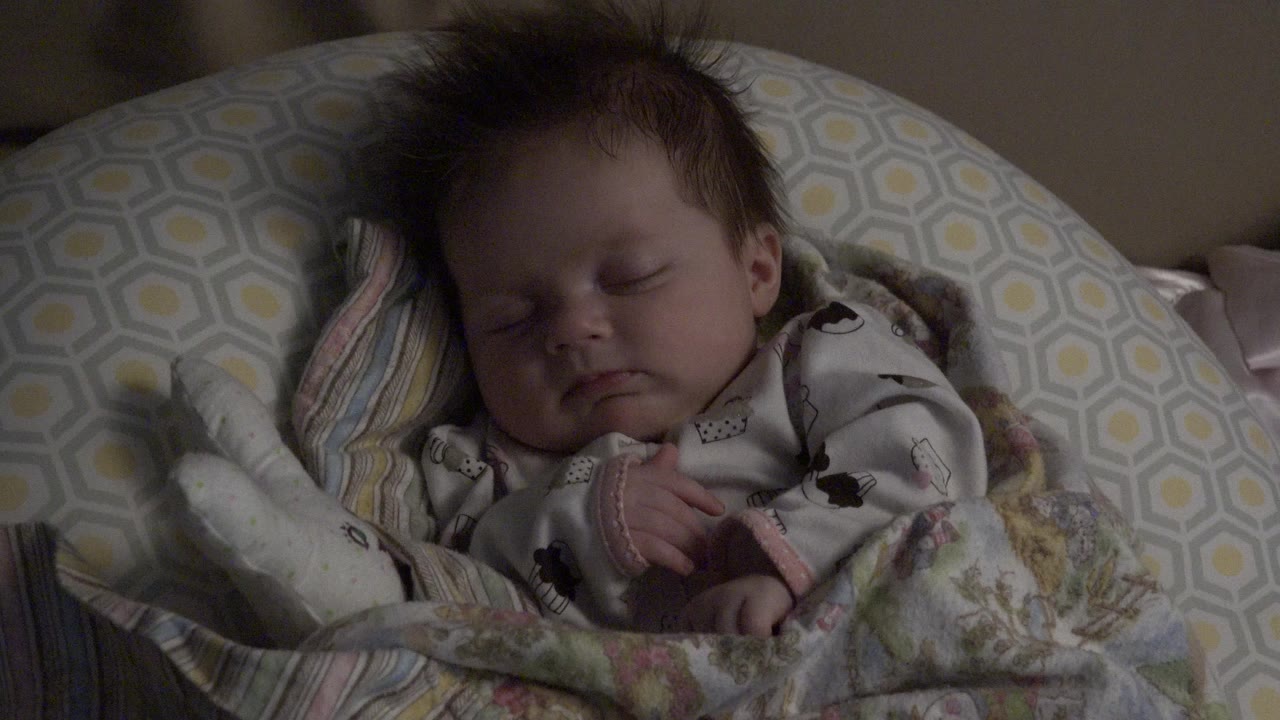 At the start of the Westminster, Colorado clip, a sleeping baby lies in a patterned rocking seat with closed eyes, tousled hair, a printed onesie, and a blanket pulled across the lower body.